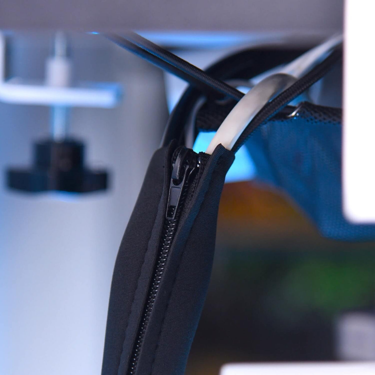 A close-up of a black zippered sleeve neatly organizing white and black cables, with a blurred background of machinery or electronics.
