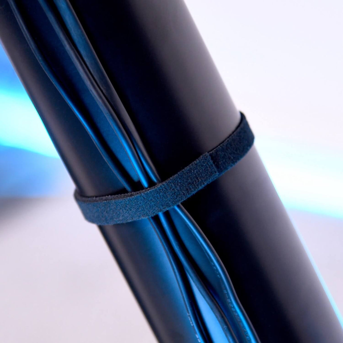 Close-up of black cables bundled together with a black Velcro strap, set against a light blue and white background.