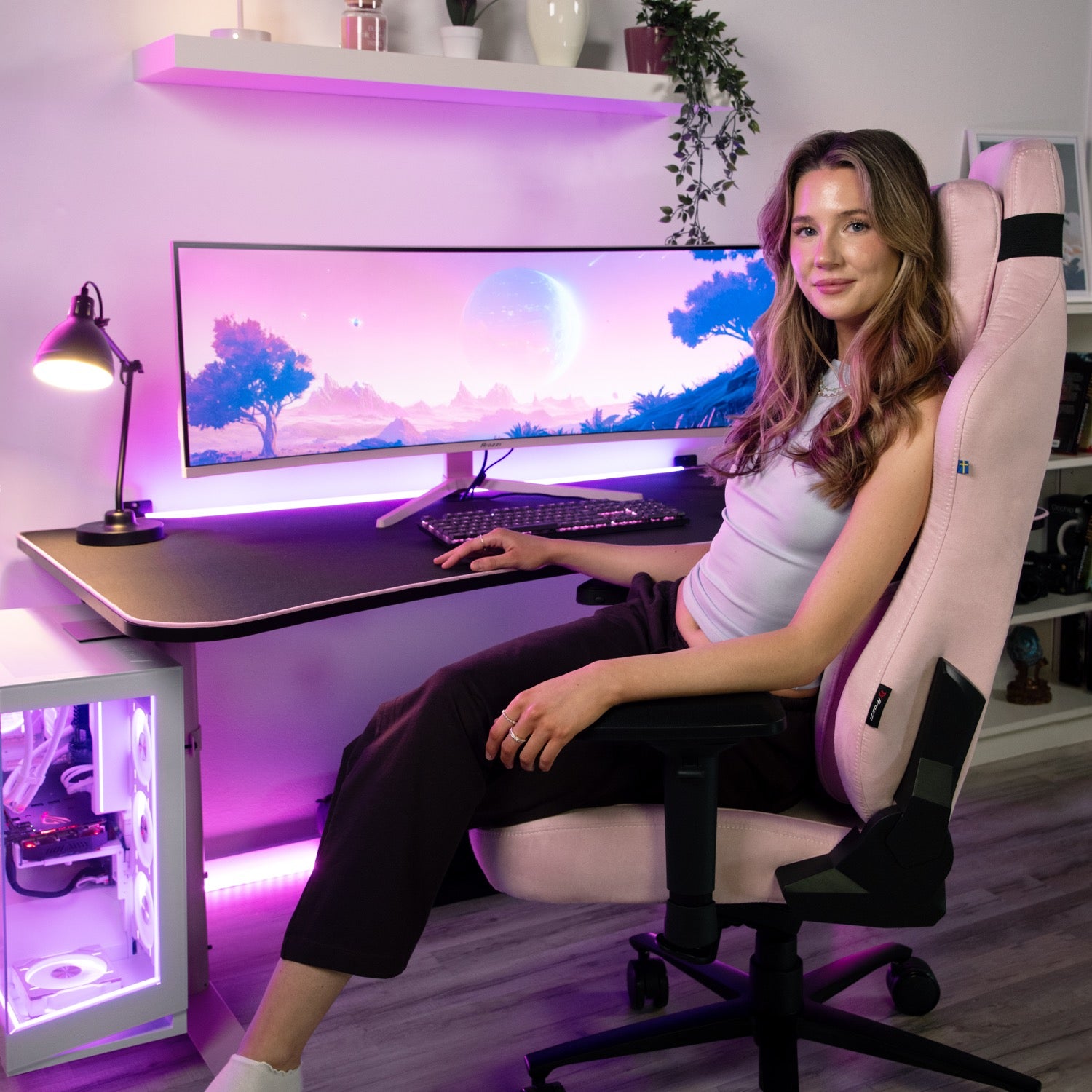 A woman sits in a pink gaming chair at a desk with the Arozzi Nova 49″ Curved VA 165Hz Ultrawide Gaming Monitor, which displays a vibrant purple sci-fi landscape. The room features modern decor and soft purple lighting, perfectly complementing the immersive visuals enhanced by adaptive sync technology.